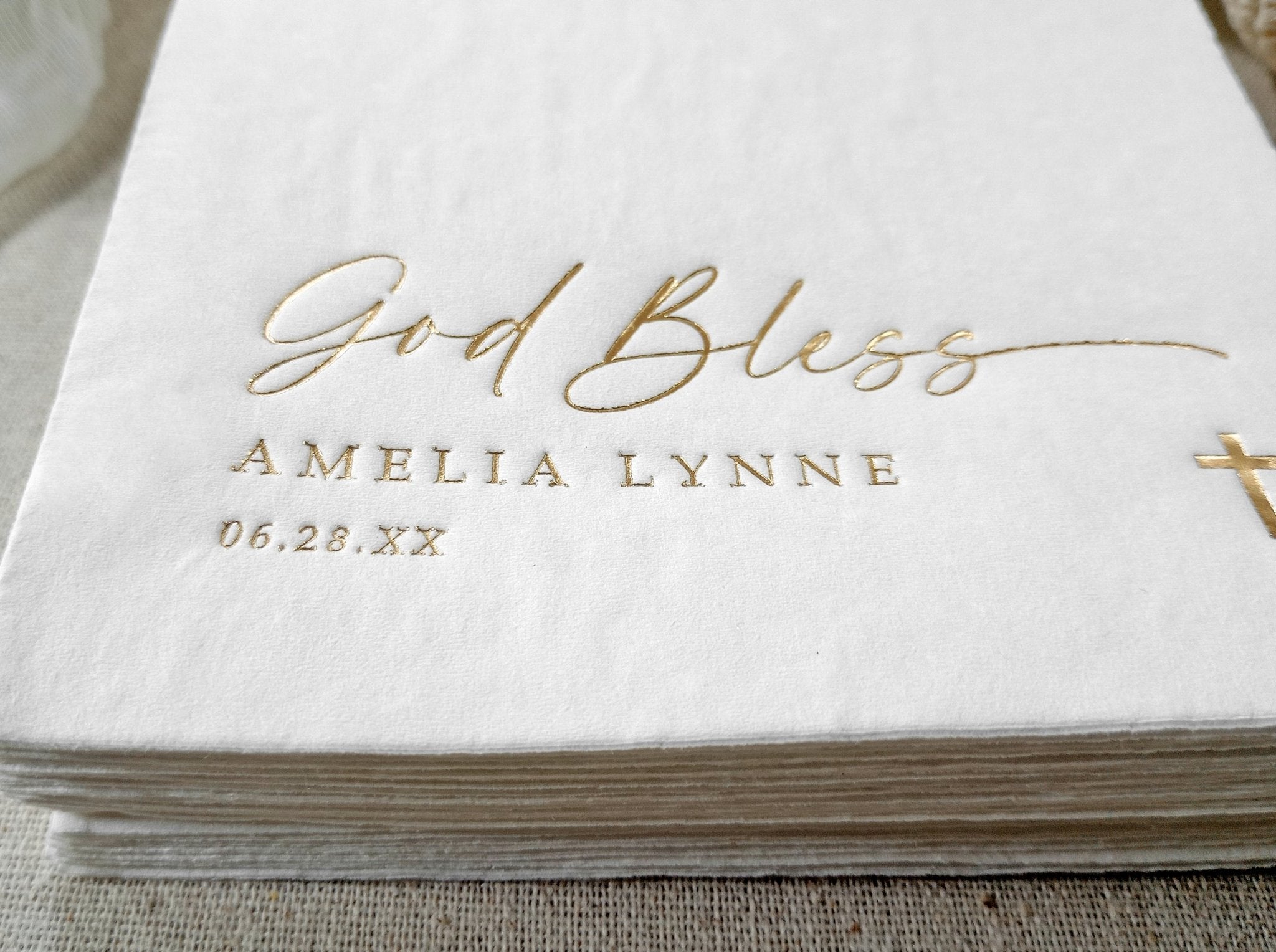 Close-up of foil-stamped “God Bless” and custom name/date on white napkin.
