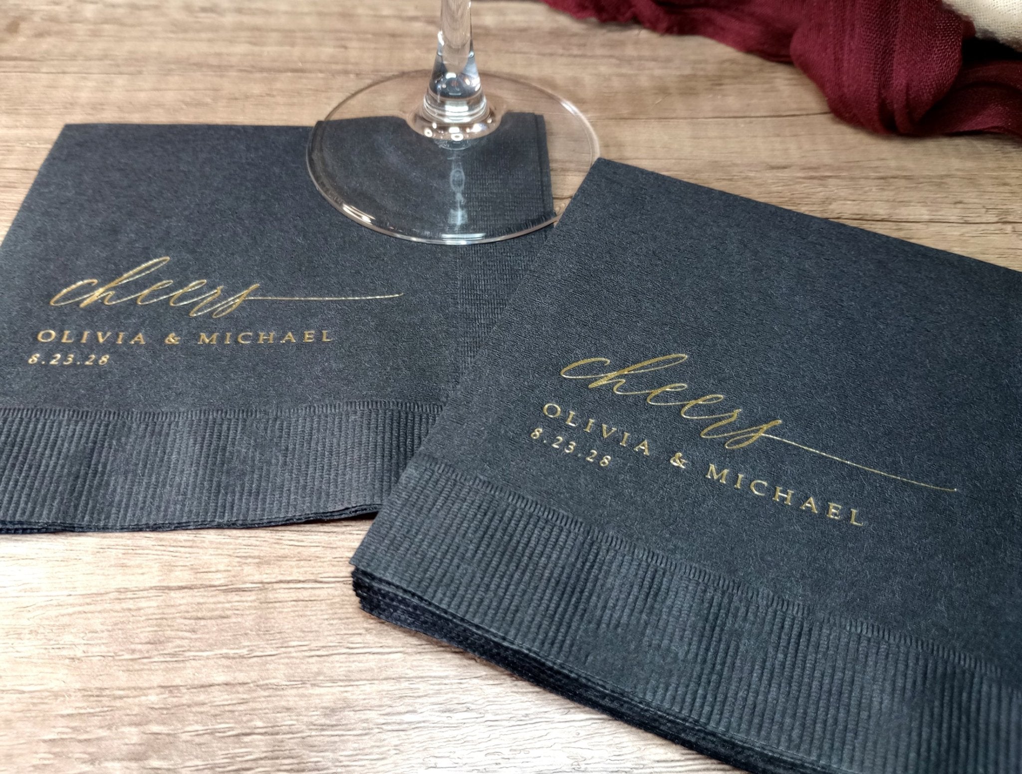 Black cocktail napkins with 'cheers' and personalized names on a wooden table.