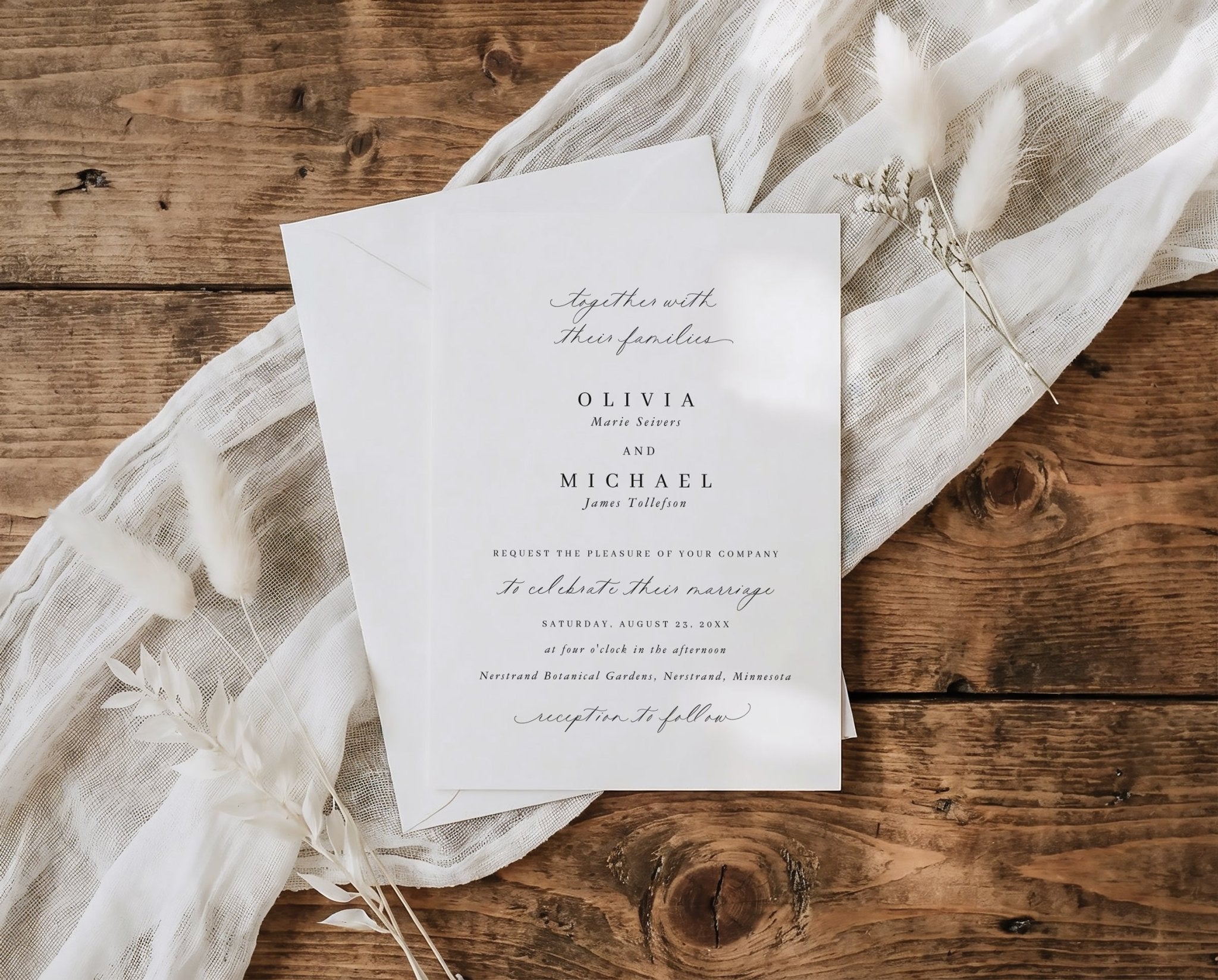 Traditional wedding invitation card on a wooden surface with delicate white fabric and flowers.