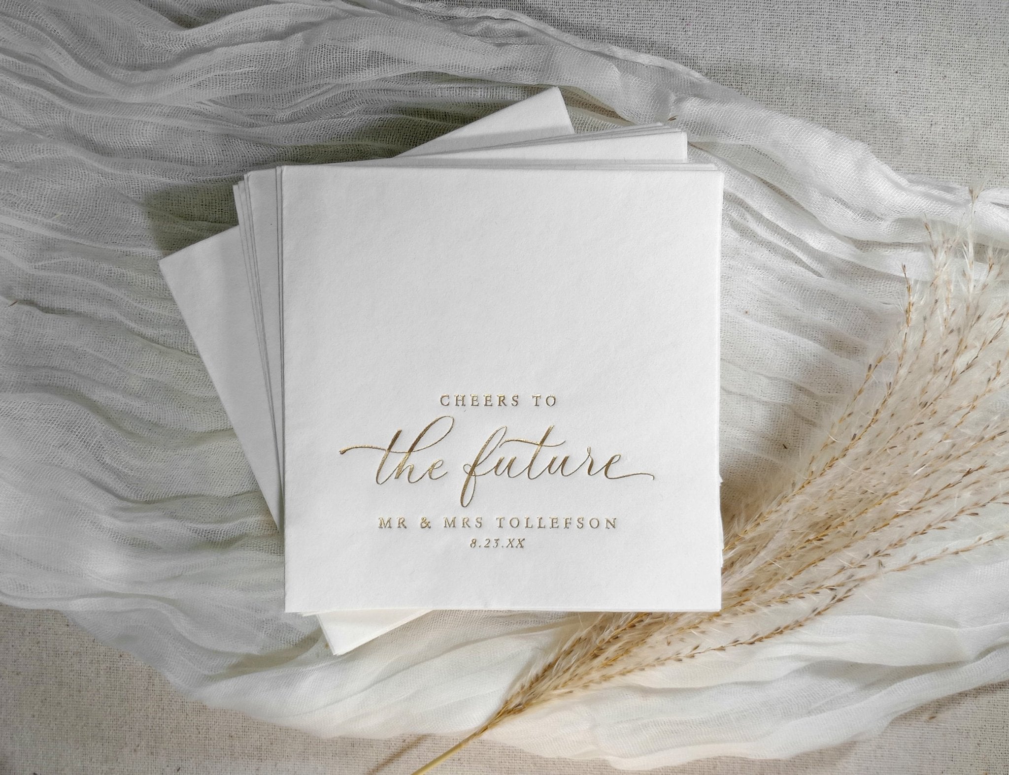 Elegant gold cocktail napkin with “cheers to the future” in modern calligraphy script.