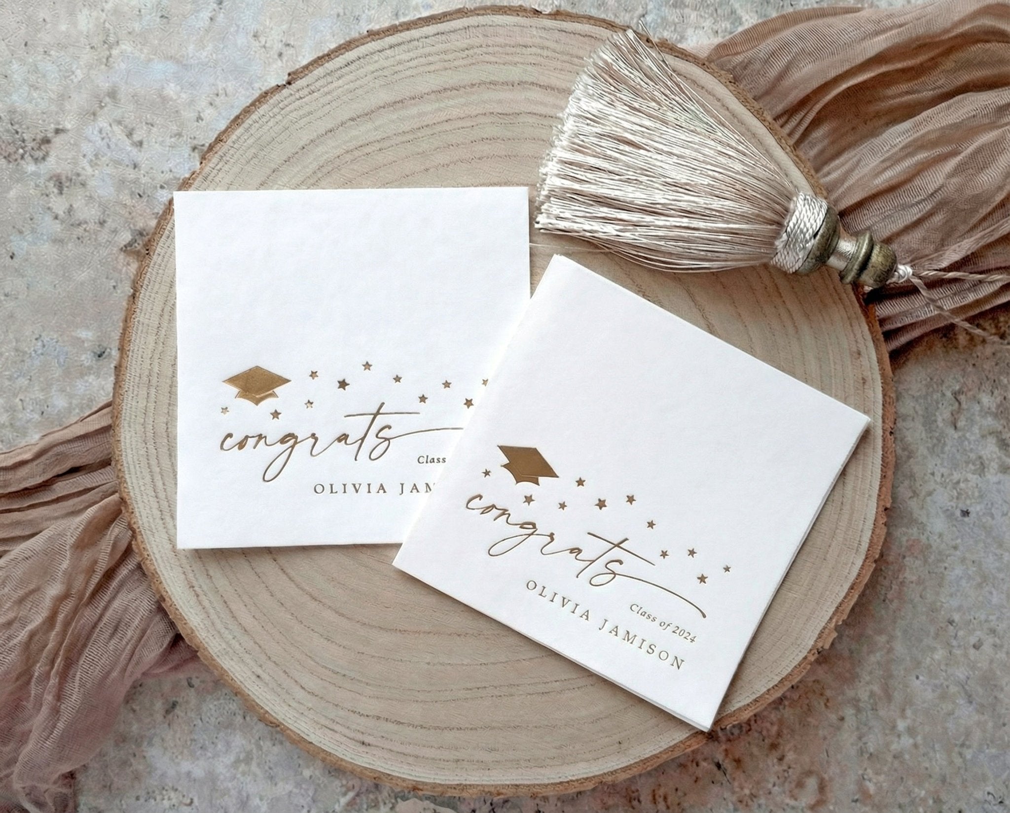 Two modern congrats graduation napkins on a wooden surface with decorative tassels.