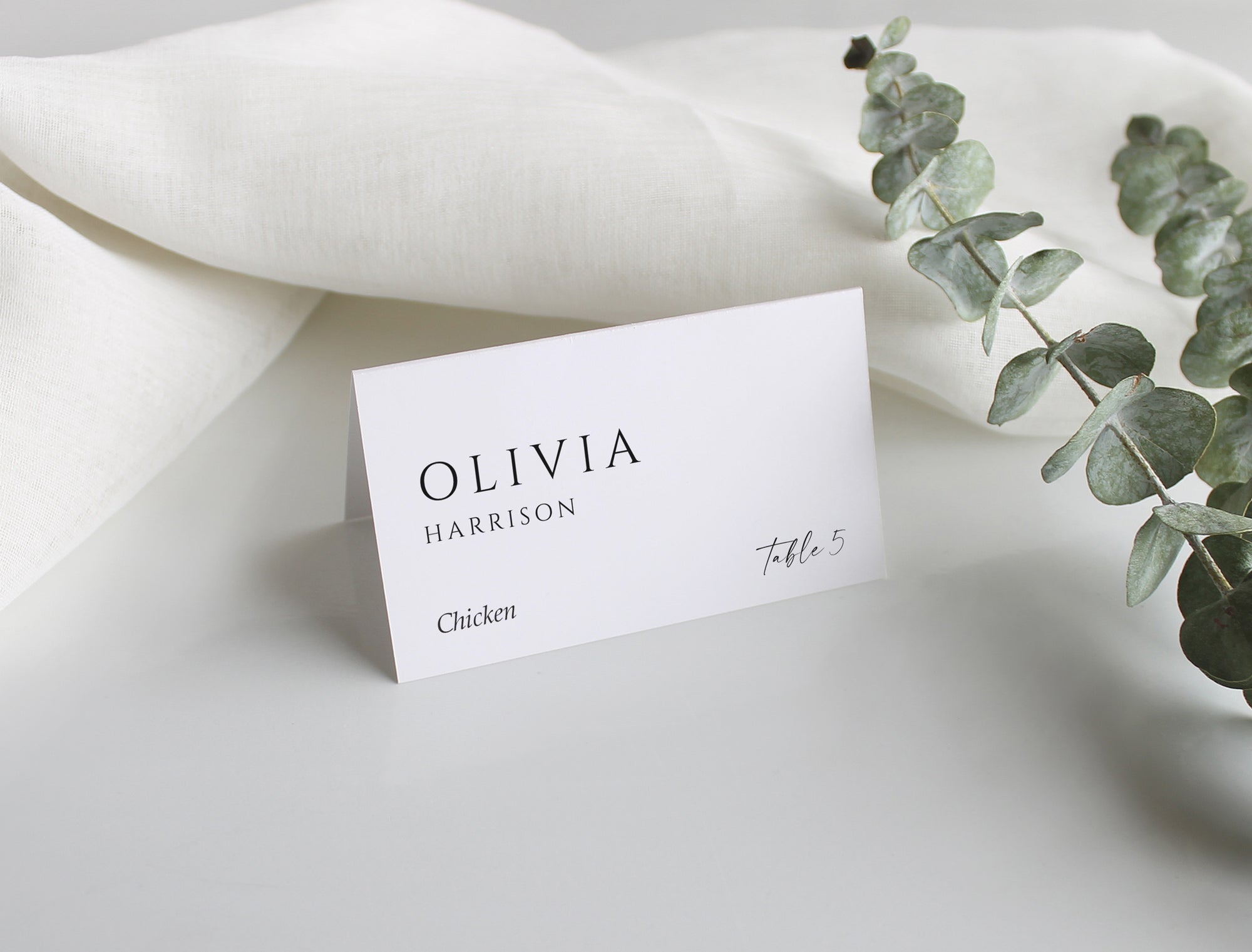 Elegant personalized wedding tent card on soft fabric with eucalyptus accent