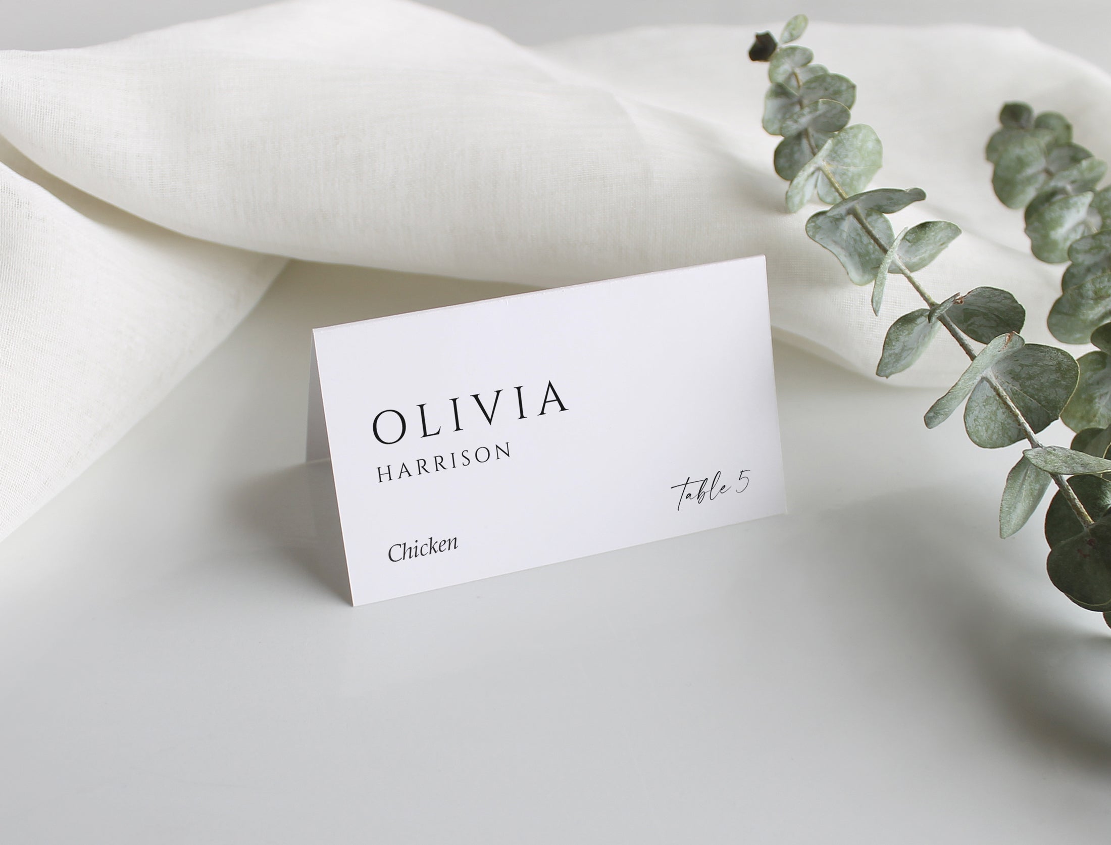 Elegant personalized wedding tent card on soft fabric with eucalyptus accent