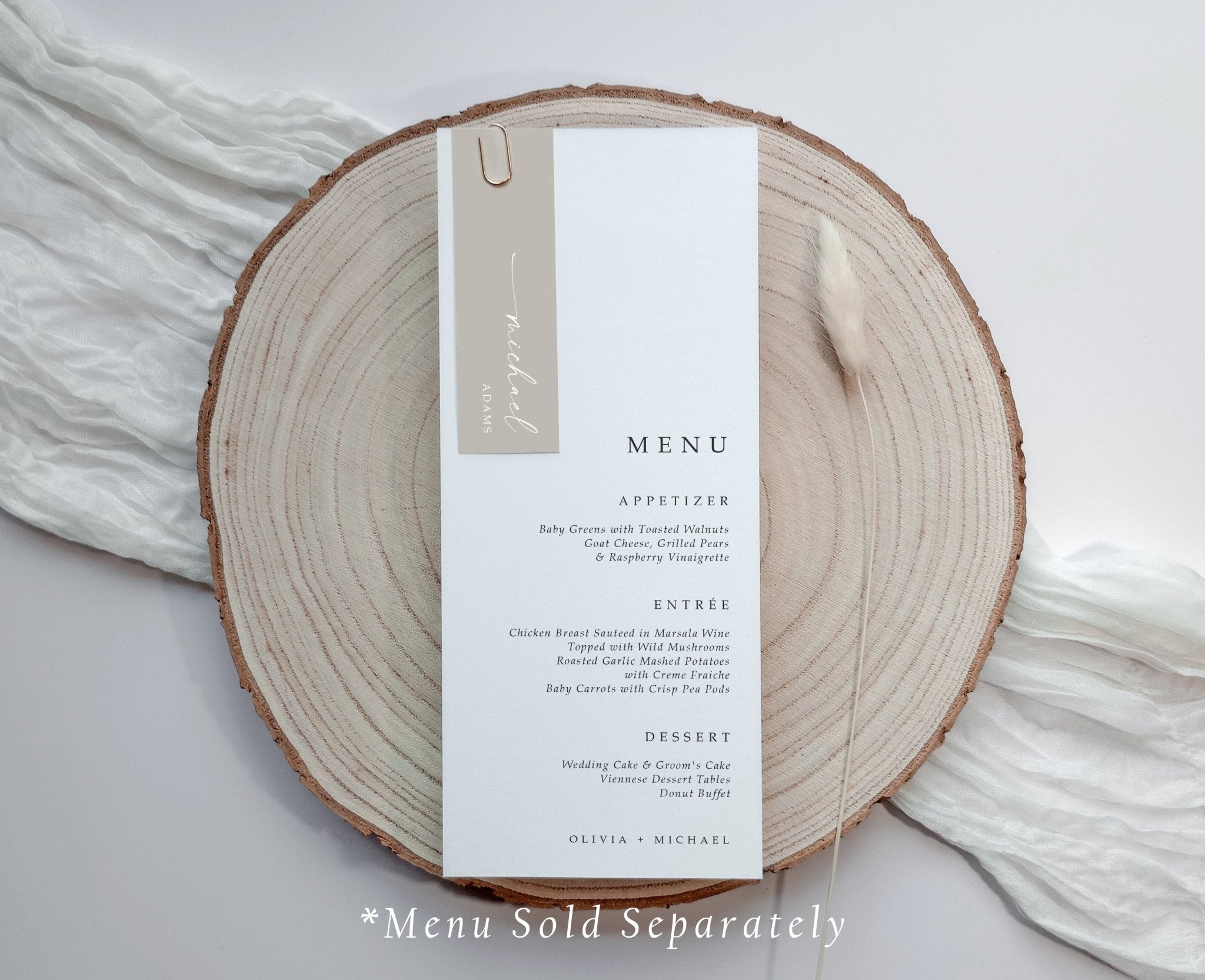 Modern wedding menu styled with taupe-colored name tag clipped on, shown on gauze with wood base.