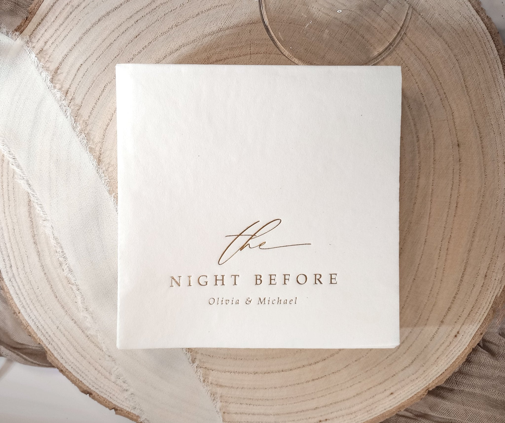 White rehearsal dinner napkin stamped in gold foil with the words ‘the night before’ and personalized names below.
