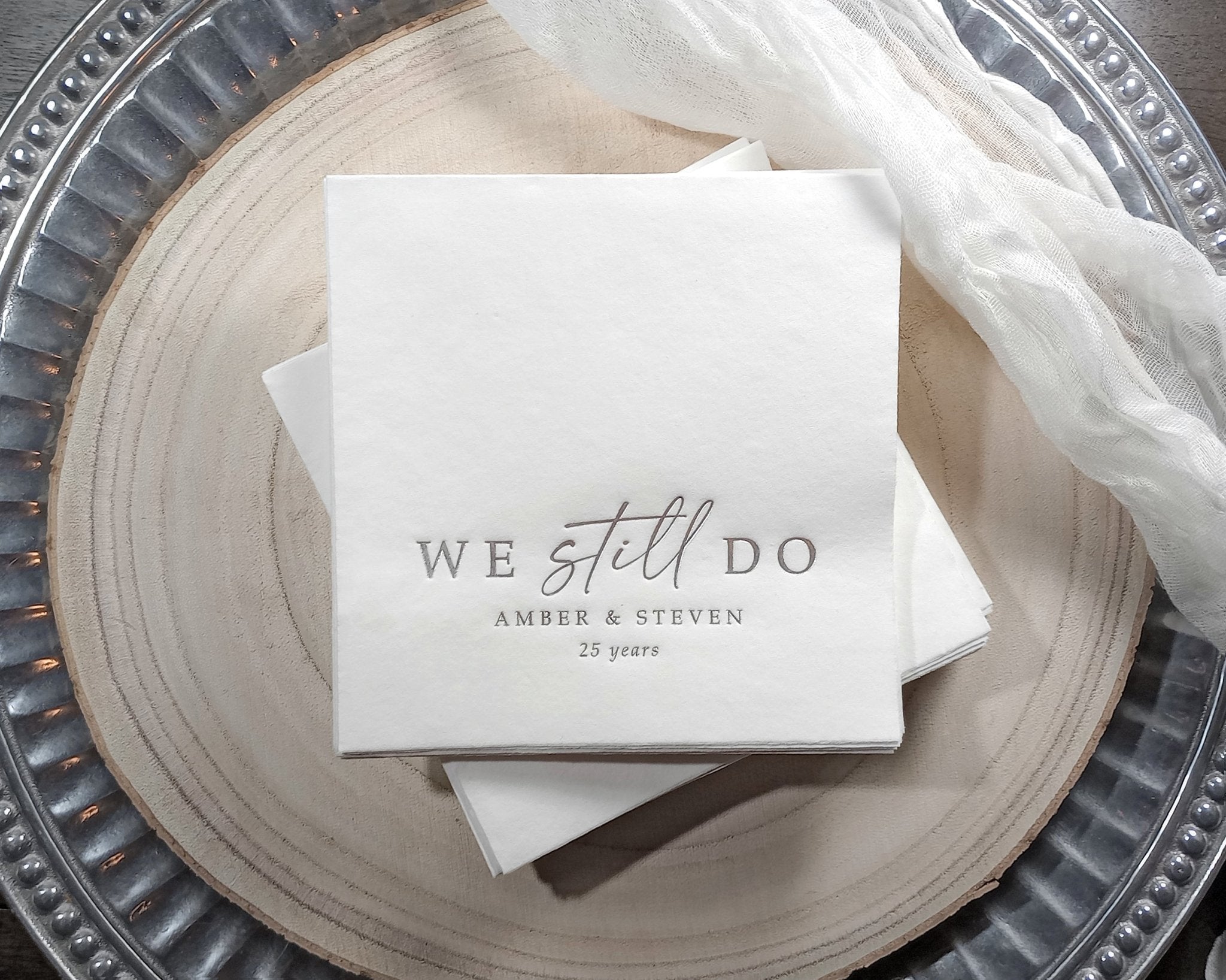 white cocktail napkins with silver foil text reading “We still do” personalized with names