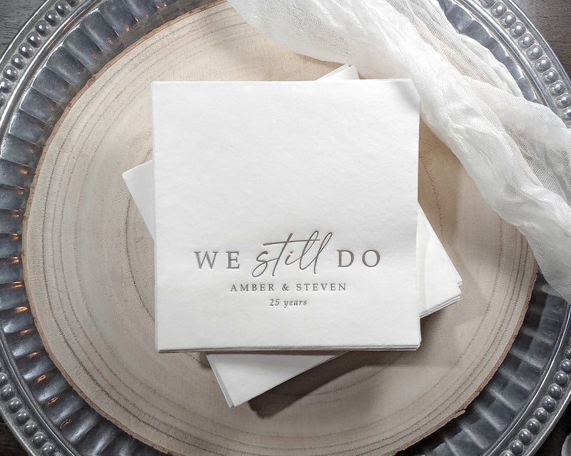 white cocktail napkins with silver foil text reading “We still do” personalized with names