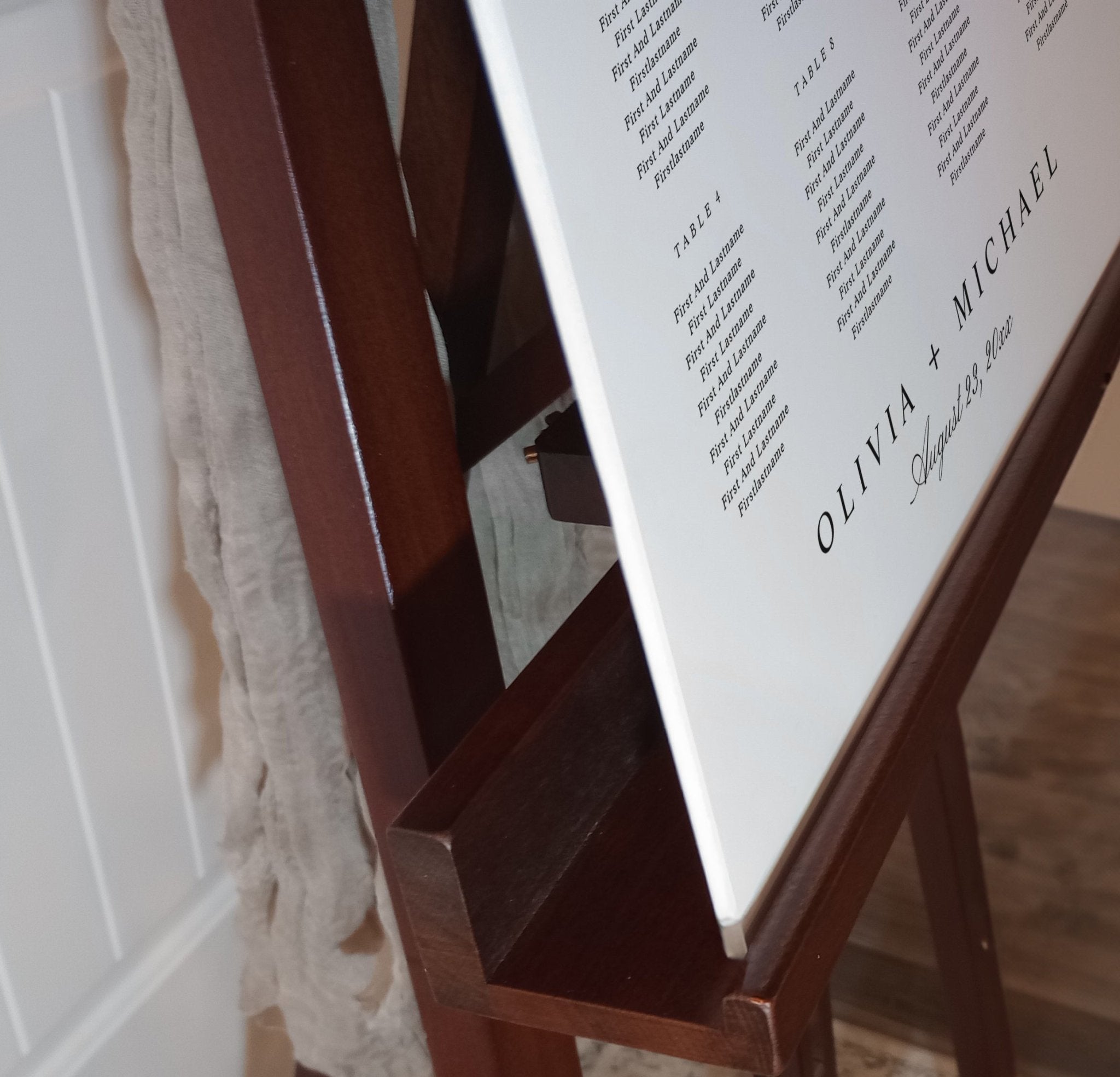 Wooden easel with a white board displaying text, a wedding seating chart, against a neutral background.
