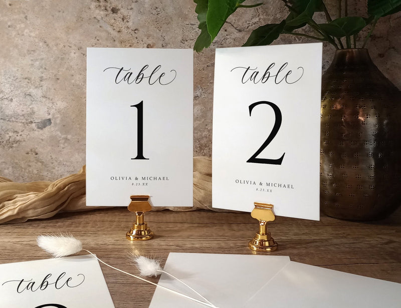 Two table number signs on a wooden surface with decorative elements.