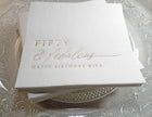 Gold foil “Fifty & Fabulous” birthday napkin with personalized name on clear glass plate