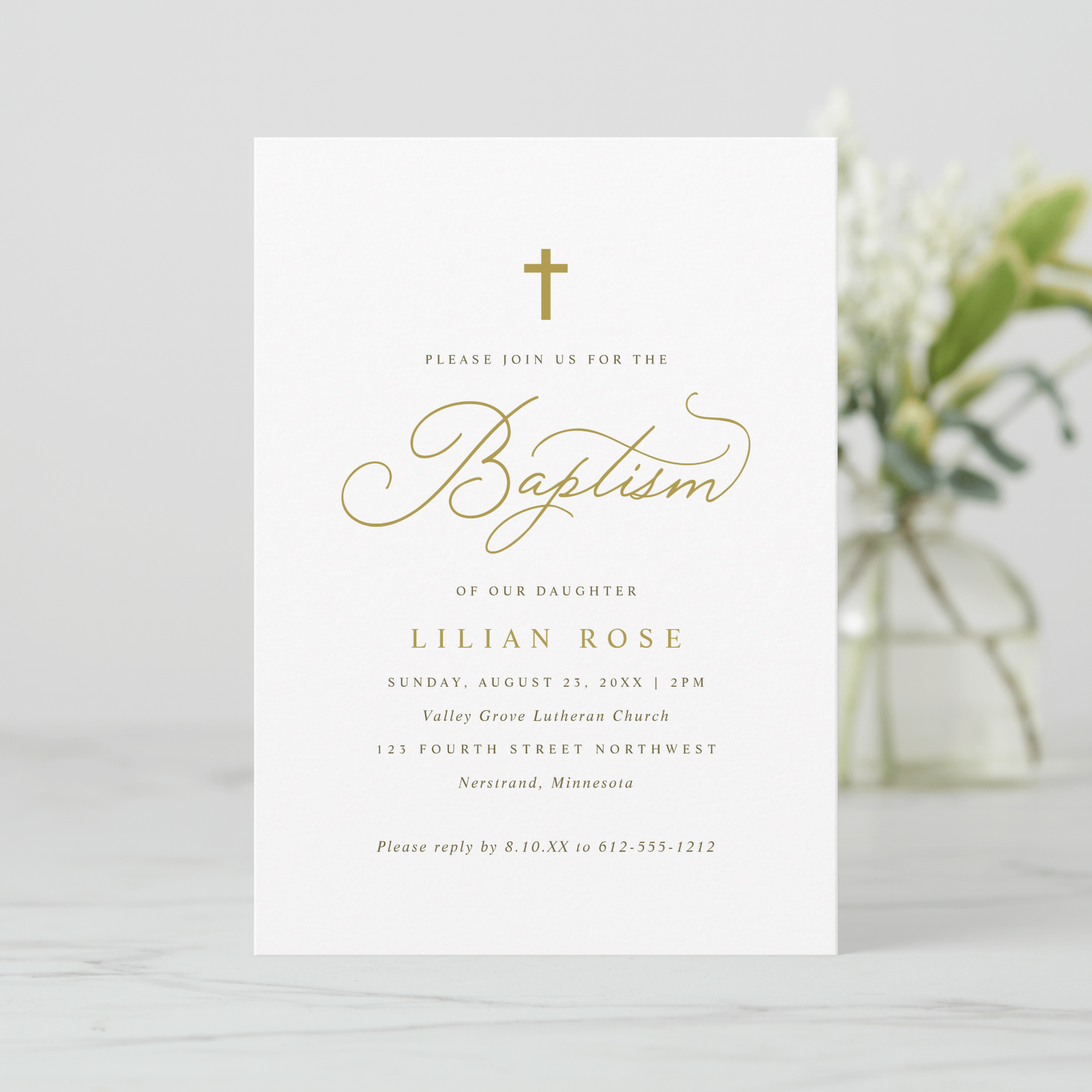 Baptism invitation card with gold text on a white background, blurred flowers in the background.