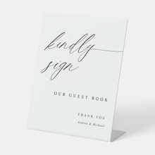 Elegant calligraphy guest book sign reading “Kindly Sign,” styled with floral wedding décor.