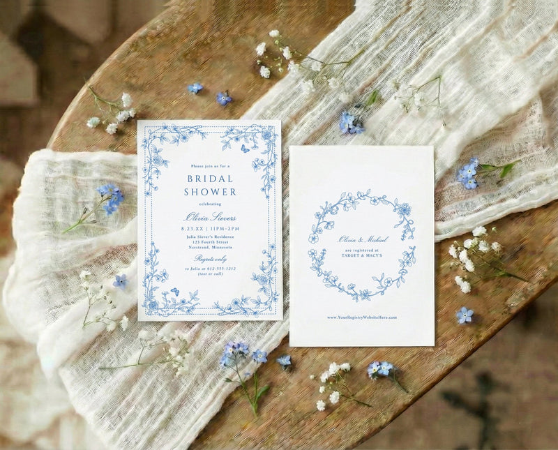 Blue and white wildflower bridal shower invitations with French vintage toile corner florals on a wooden surface.