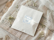 White envelope with a blue floral label on a textured fabric background