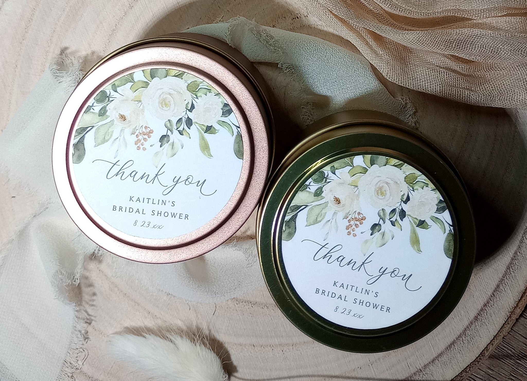 Two small tin containers with floral labels for a bridal shower on a soft fabric background.