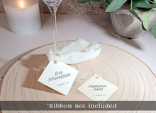 minimalist wedding glass tags with guest names and table numbers tied with ribbon
