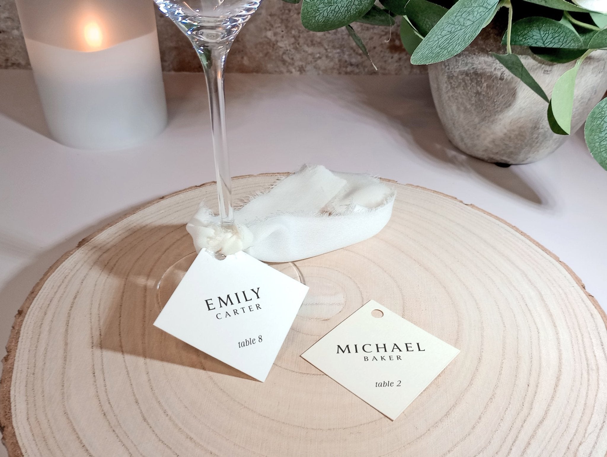 Diamond-shaped name tags tied to champagne glass stems with guest names and table numbers.