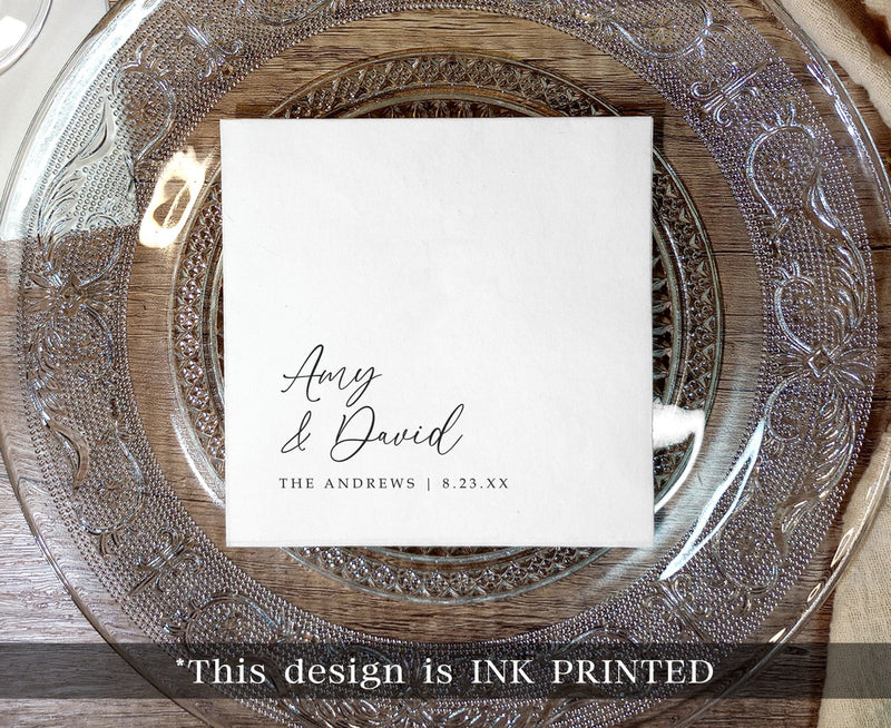black ink printed wedding napkin with names in elegant handwriting script on clear charger plate