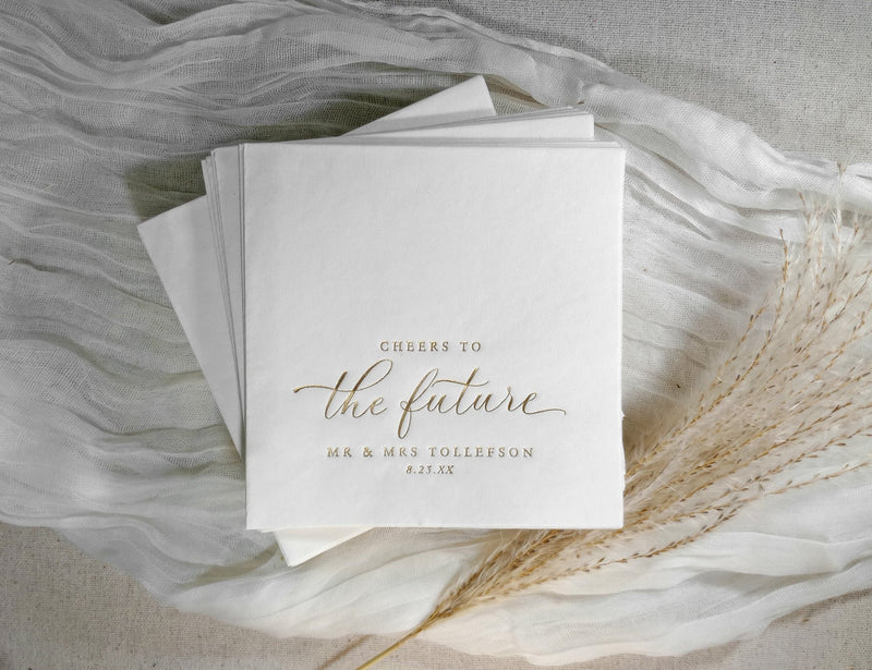 Elegant gold cocktail napkin with “cheers to the future” in modern calligraphy script.
