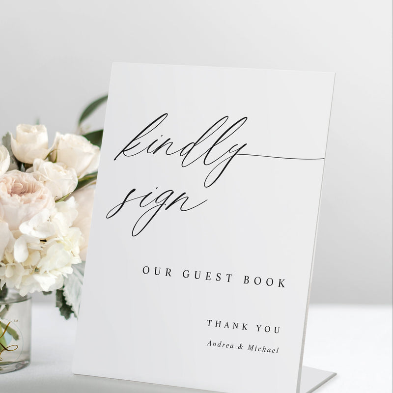 Standing “Kindly Sign our Guest Book” wedding guest book sign in romantic calligraphy, displayed on a reception table.