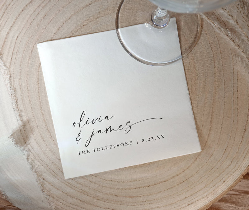 A square white paper personalized black and white wedding napkin with elegant black script reading 'olivia & james' and smaller text 'THE TOLLEFSONS | 8.23.
