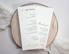 A wedding menu and thank you card set printed on white cardstock, styled on a round natural wood slice with soft white fabric in the background.