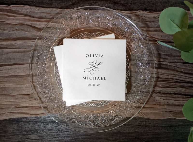 White napkins with 'Olivia and Michael' on an elegant decorative glass plate with a wooden background