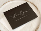 Black card with 'thank you' and personalized text on a wooden surface