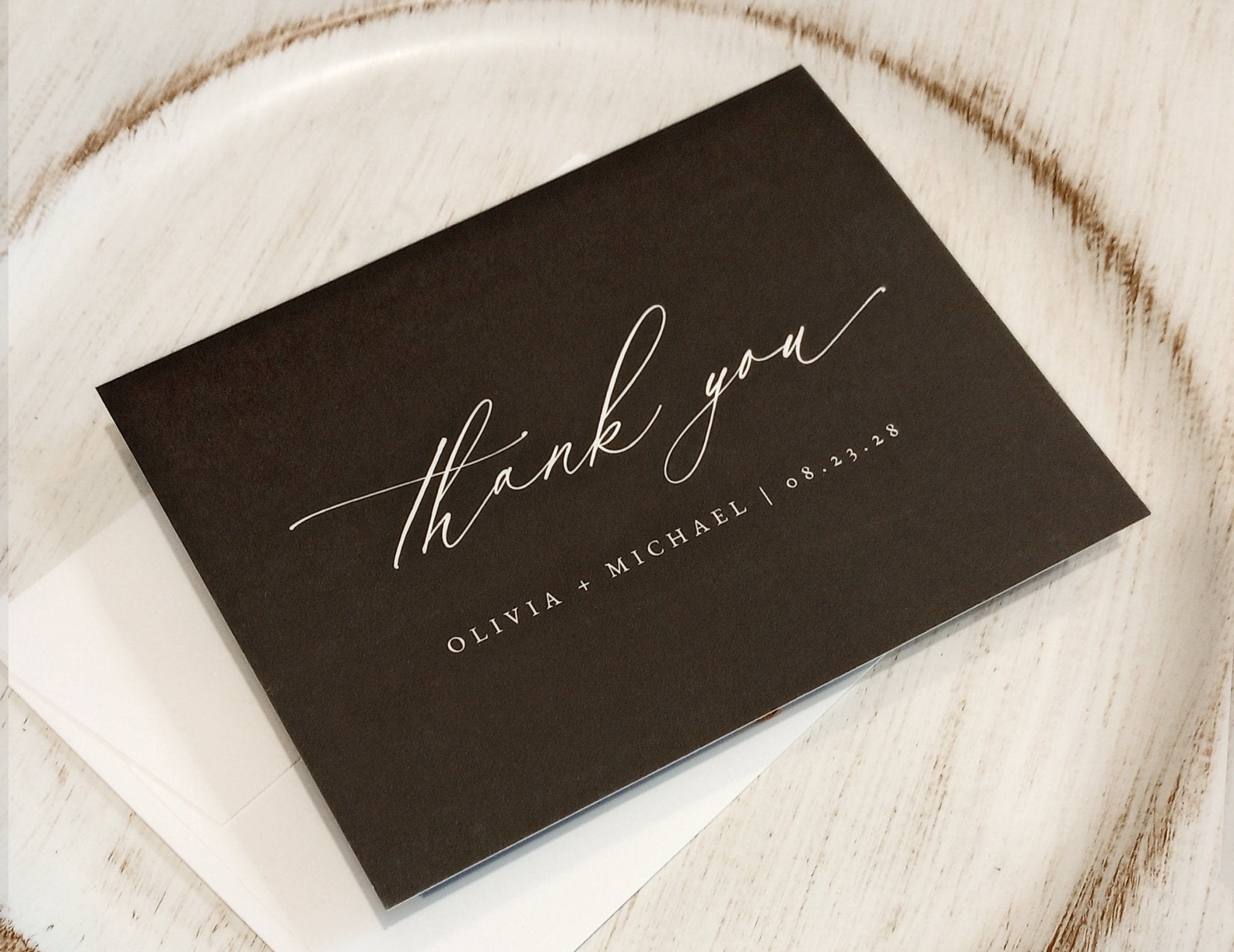 Black card with 'thank you' and personalized text on a wooden surface