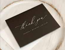 Black card with 'thank you' and personalized text on a wooden surface
