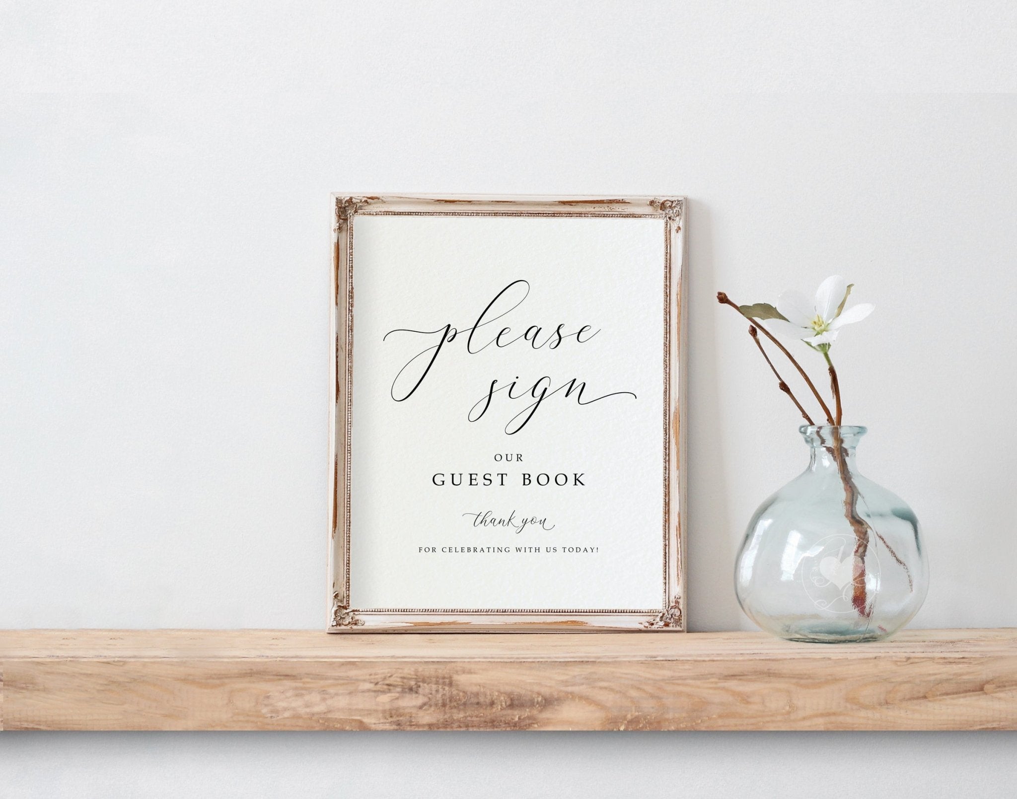 Framed guest book sign on a wooden shelf with a vase containing a plant