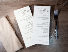 Two wedding menus on a wooden table with a fork and beige napkin.