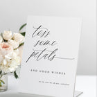 Standing “Toss Some Petals” wedding sign in modern calligraphy, displayed with a bouquet and petals.