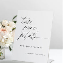 Standing “Toss Some Petals” wedding sign in modern calligraphy, displayed with a bouquet and petals.