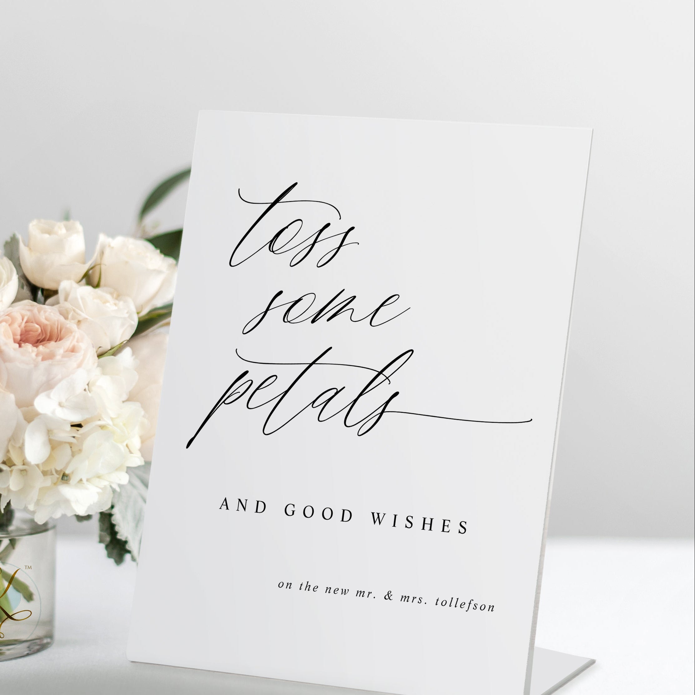 Standing “Toss Some Petals” wedding sign in modern calligraphy, displayed with a bouquet and petals.
