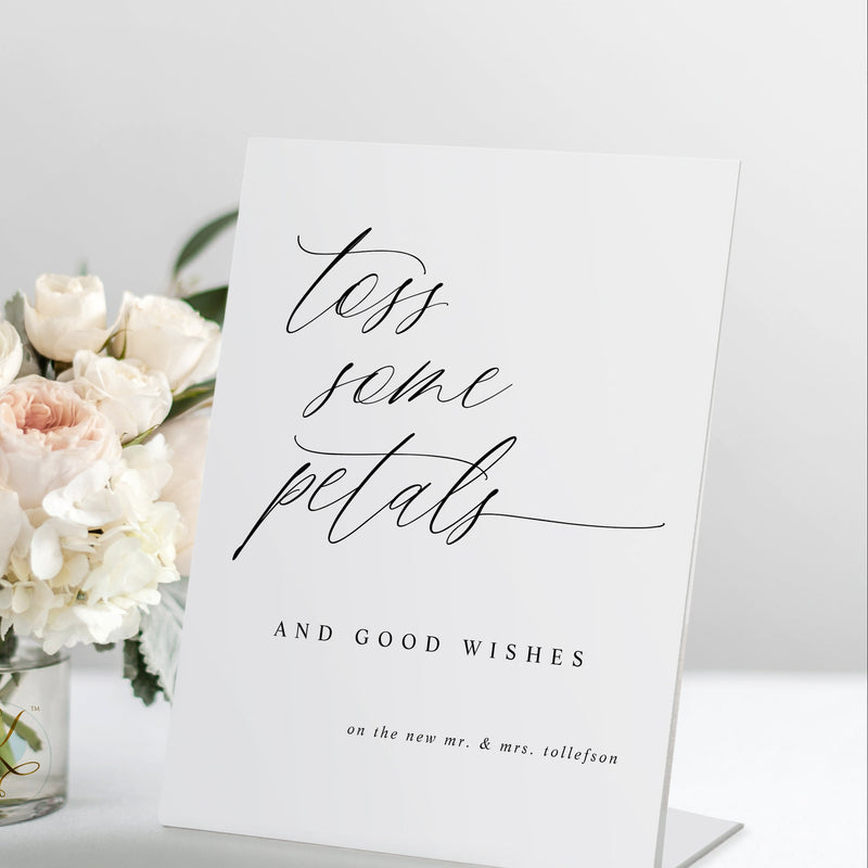 Standing “Toss Some Petals” wedding sign in modern calligraphy, displayed with a bouquet and petals.