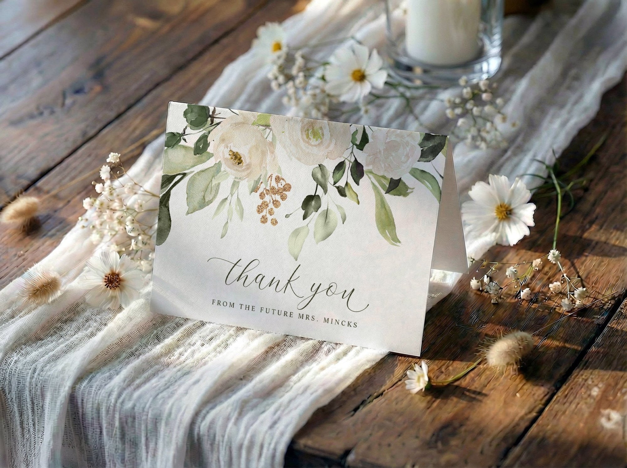 Bridal shower thank you card with floral design on a wooden table with flowers and a candle.