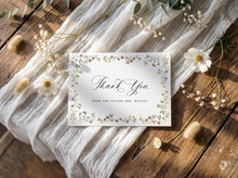 Thank you card with wildflower floral design on a wooden surface with white fabric and flowers.