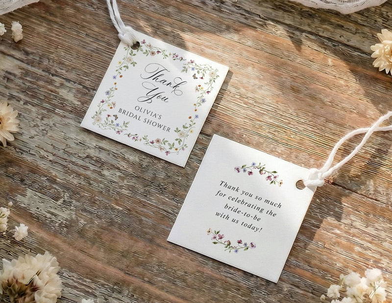 Two small favor tags with floral designs on a wooden surface with dried flowers.