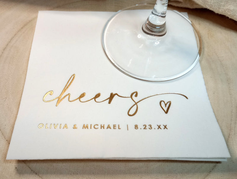 Personalized napkin with 'cheers' and names on a wooden surface