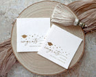 Two modern congrats graduation napkins on a wooden surface with decorative tassels.