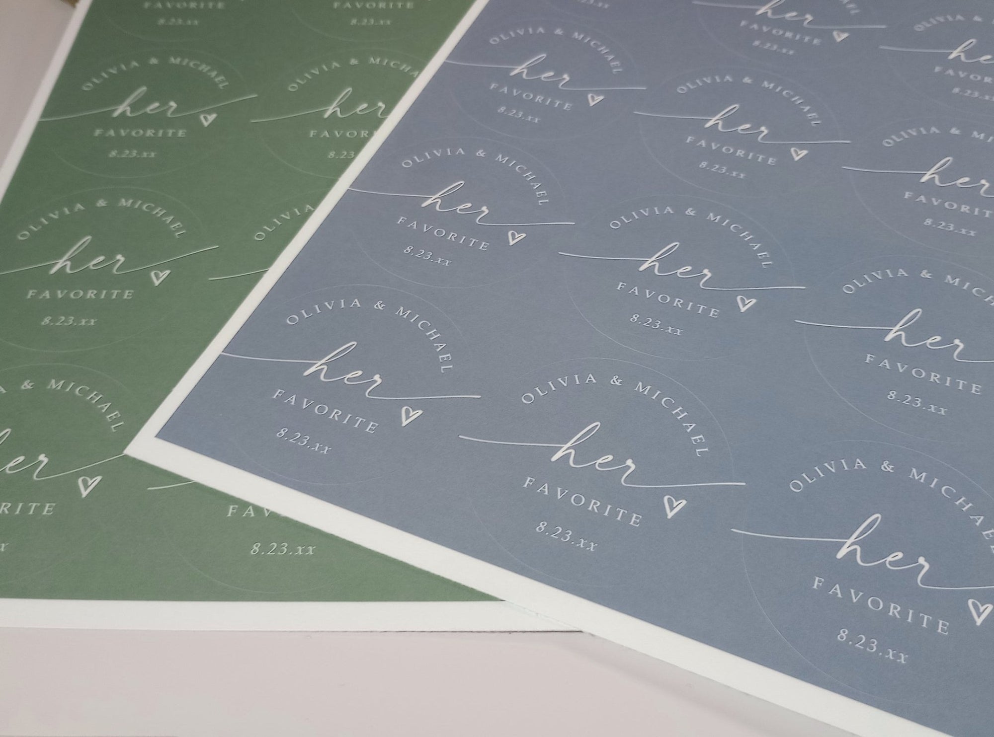 Two sheets of stickers in dusty blue and sage with 'her favorite' text on a white background