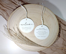 Two round white tags for guest hotel bags with 'welcome' text on a wooden surface