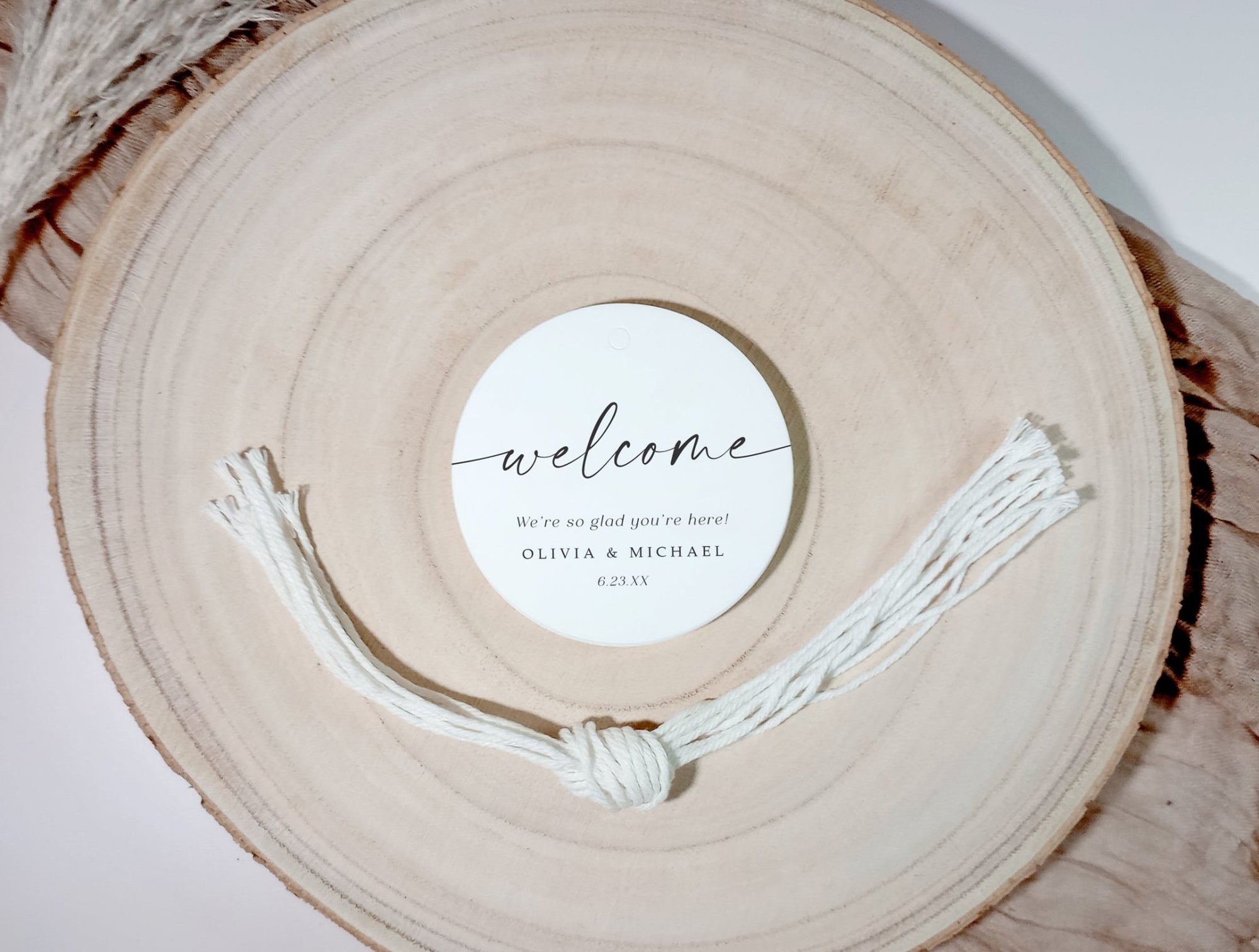 Round wooden charger with a stack of 'welcome' tags and strings on a light background