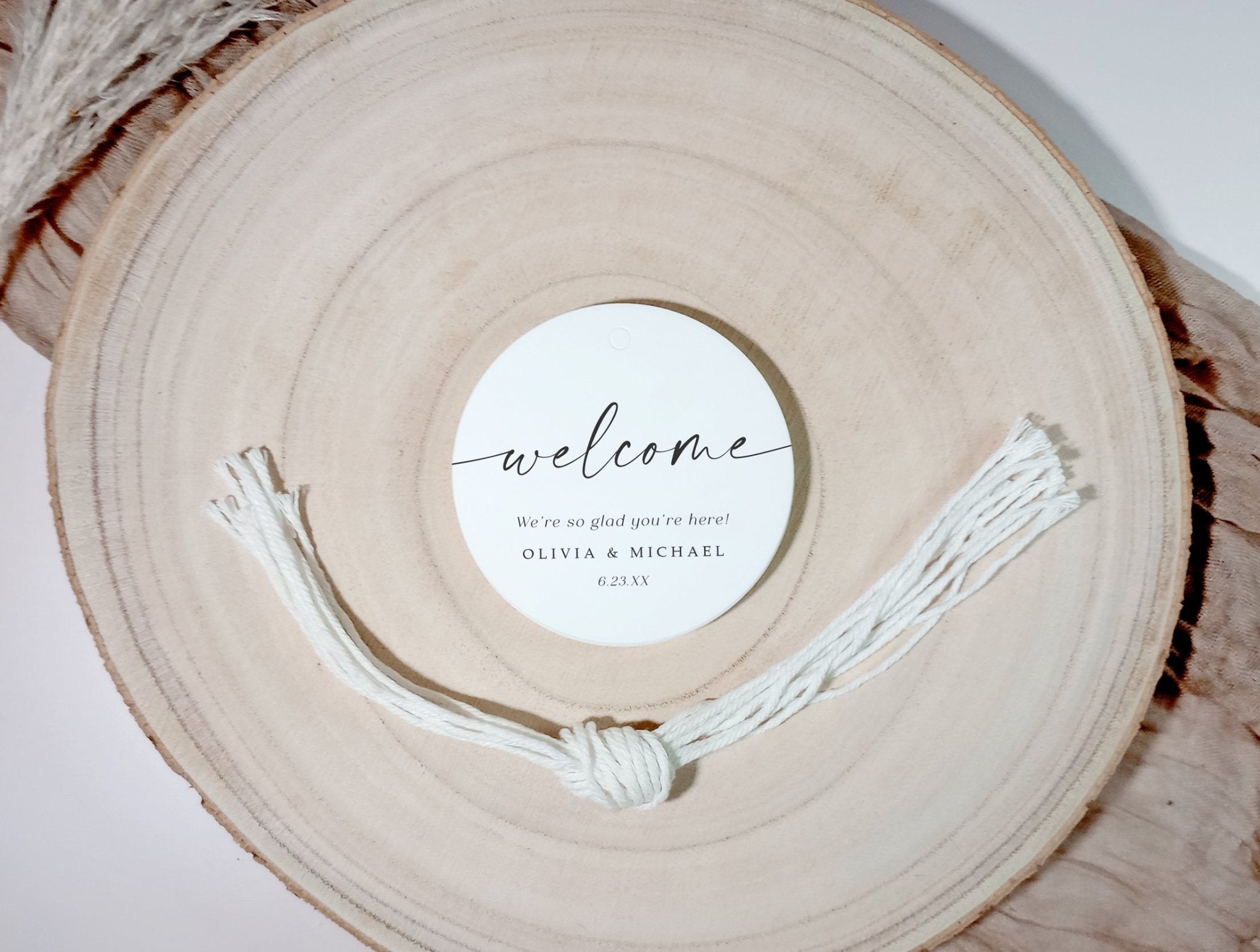 Round wooden charger with a stack of 'welcome' tags and strings on a light background