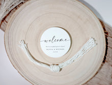 Round wooden charger with a stack of 'welcome' tags and strings on a light background