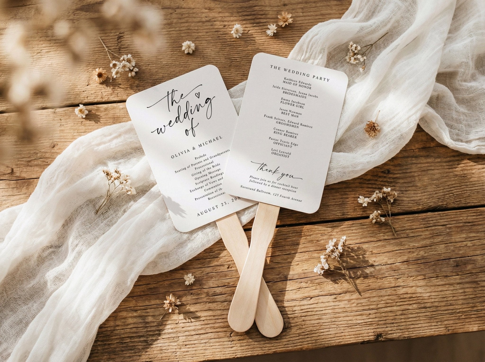 Two wedding program fans on wooden sticks with dried flowers and fabric on a wooden surface.
