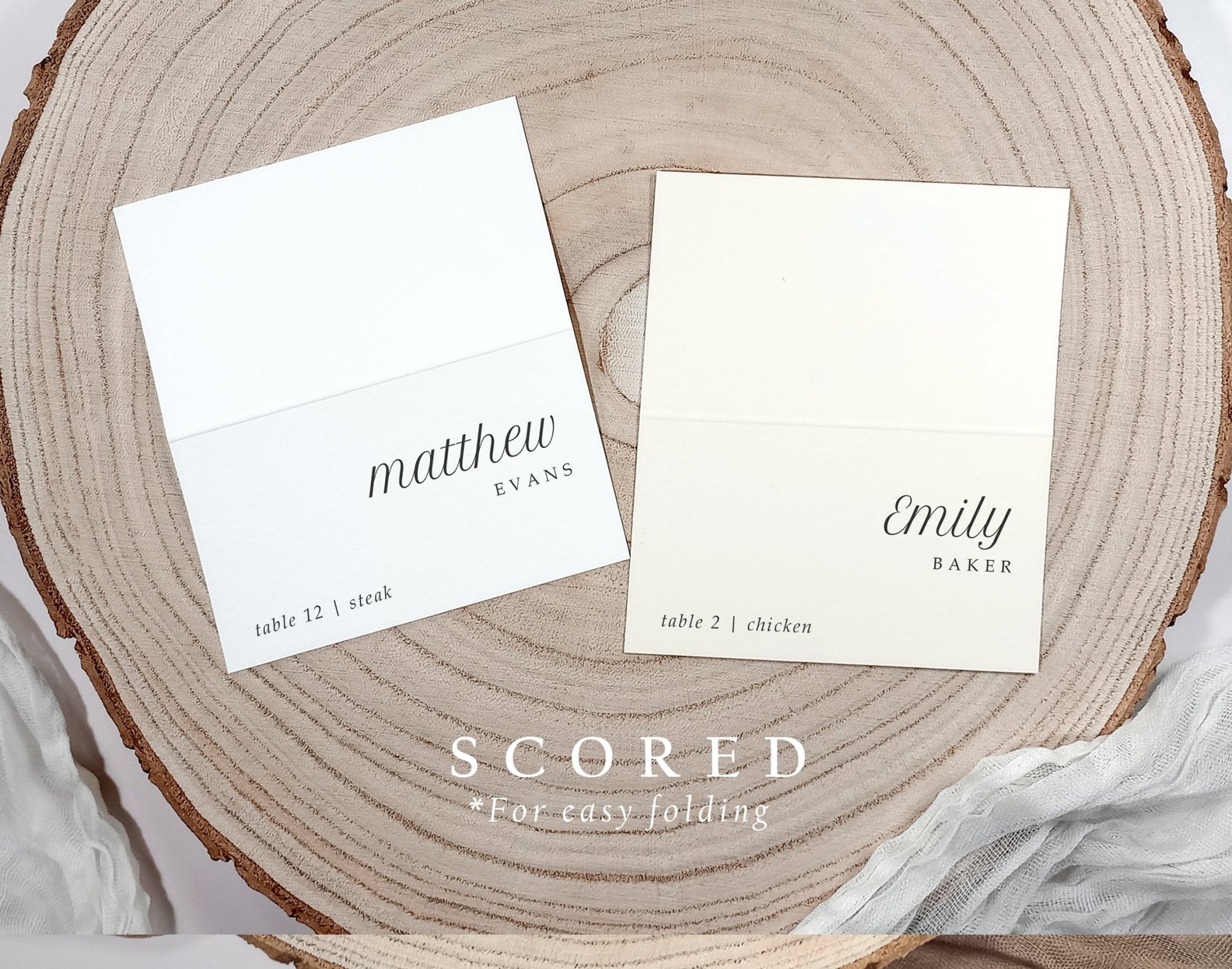 Two white name cards on a wooden surface with text 'matthew evans' and 'emily baker'.