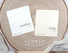 Two white name cards on a wooden surface with text 'matthew evans' and 'emily baker'.