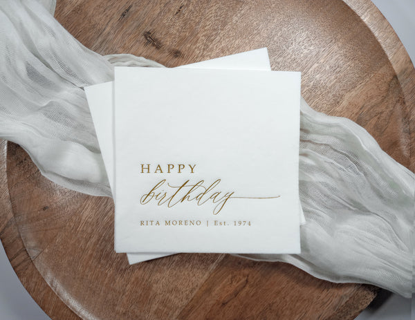 Personalized Happy Birthday napkins with name and birth year in gold foil, styled with gauze on wood round.